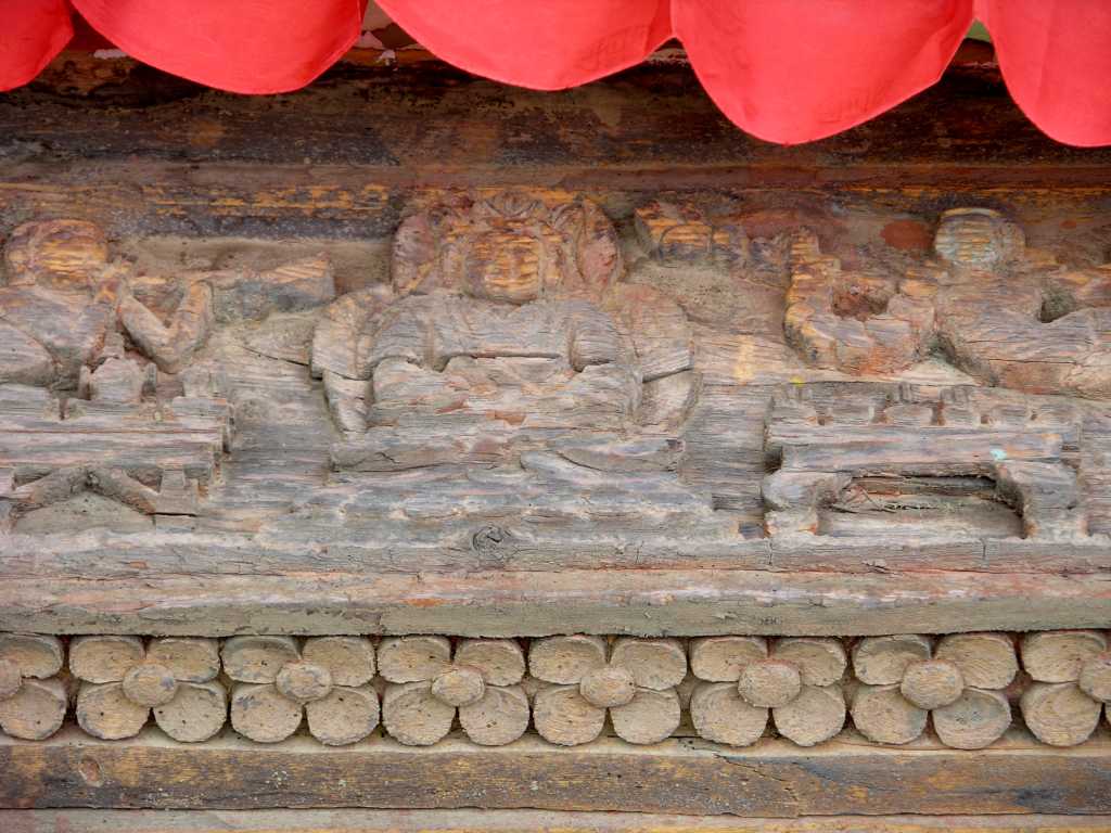 Tibet Guge 07 Tsaparang Red Temple 03 Door Carving Its pillars are sculpted with floral motifs and covered up with small figures worked out with great delicacy � Above, in a square frame, the Buddha seated in the posture of meditation; on his sides two small figures of gods who hovering in the air play the trumpet by way of homage. - Giuseppe Tucci: The Temples of Western Tibet and their Artistic Symbolism (1935).